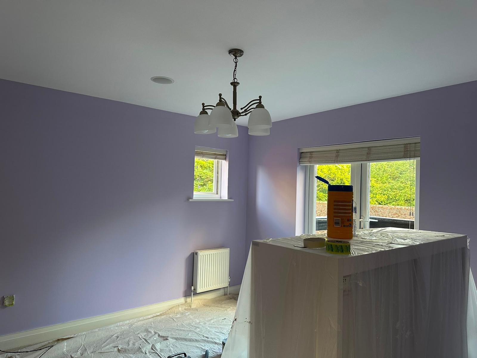 Lilac bedroom with furniture wrapped in plastic and floor covered