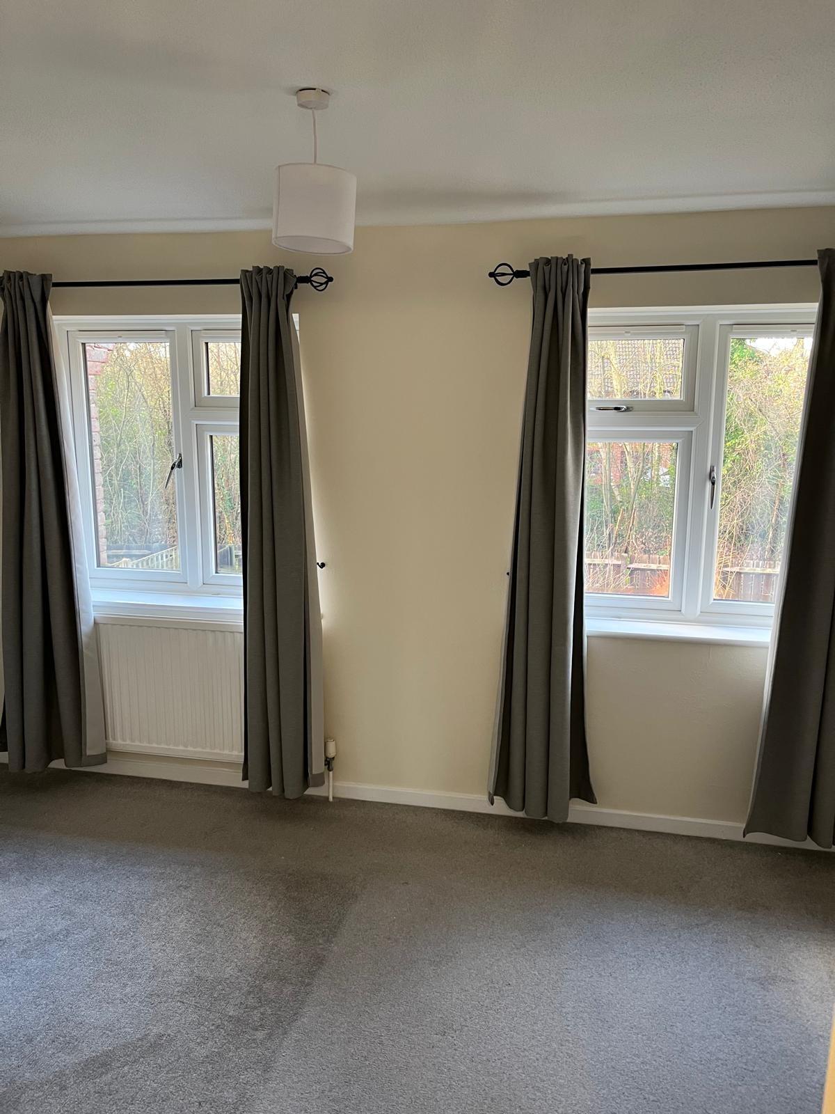 Bedroom with cream walls between two curtained windows
